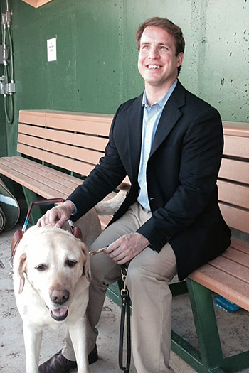 On an early summer day, Pat, in a blue sportscoat, and Galahad sit on a bench in the Nationals Youth Baseball Academy dugout.